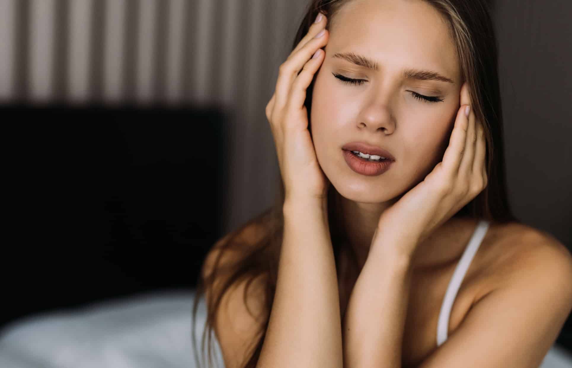 Photo d une jeune femme tenant sa tete avec ses mains les yeux fermes migraine | Dr Christophe Reinbold Lyon